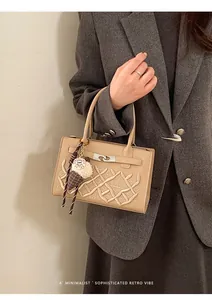 Detail of beige embossed leather handbag with GA logo and ice cream charm on grey blazer