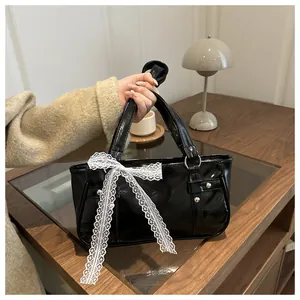 Detail of black glossy handbag with white lace bow and silver hardware on a desk