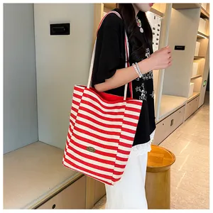 Detail of red and white striped canvas tote bag showing the metal logo plate and texture