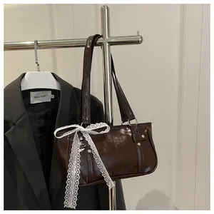 Close-up of brown glossy handbag featuring silver studs and white lace ribbon decoration