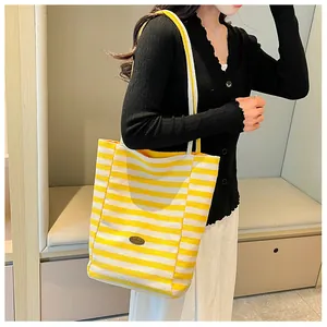 Detail of yellow and white striped canvas tote bag with a metal logo on a model