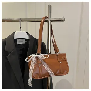 Detail of a brown glossy leather shoulder bag with white lace bow and silver rivets