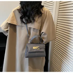 Detalle de bolso trapecio gris oscuro con cierre dorado y correa ajustable en una modelo