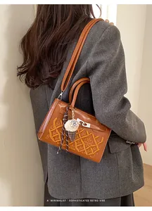 Detail of brown leather bag with yellow embroidery and plush charm on a gray blazer