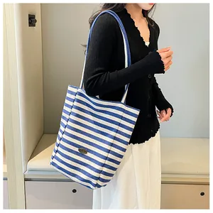Detail of blue and white striped canvas tote bag showing the metallic brand plate and strap