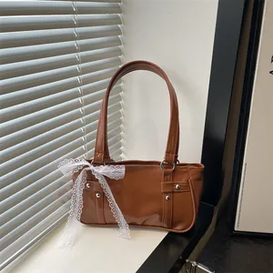 Brown vintage baguette bag with white lace bow detail and silver studs in natural light