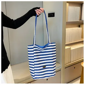 Detail of blue and white striped canvas tote bag with long shoulder straps and metal logo