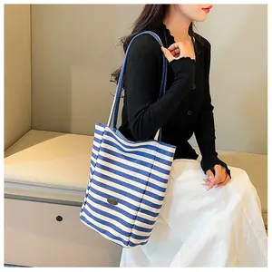 Close-up of blue and white striped canvas tote with adjustable strap and metal logo
