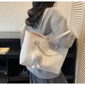 Detalle del bolso tote blanco con textura floral en relieve y colgante de nube suave