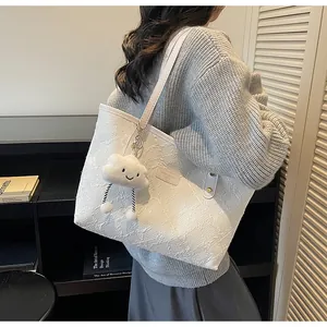 Detalle del bolso tote blanco texturizado con placa de marca y charm de nube de peluche