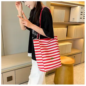 Detail view of red and white striped canvas tote bag with metal nameplate and shoulder strap