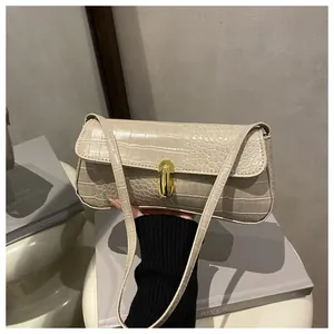 Close-up of cream faux crocodile texture and gold metal bar lock on a sleek baguette bag