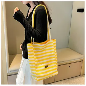Detail of a large yellow and white striped canvas tote bag with metal logo on model