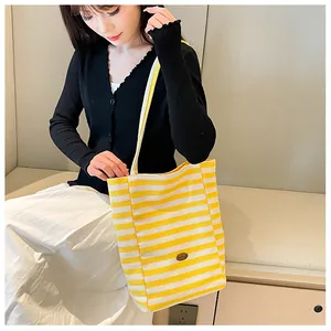 Detail of yellow and white striped canvas tote bag with oval logo patch on model