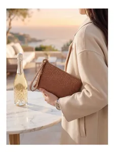 Close-up of brown woven leather clutch with metal zipper and wrist strap on a terrace