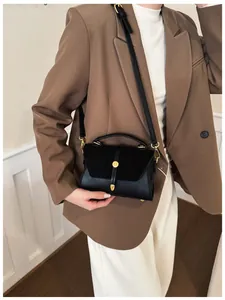 Detail der schwarzen Leder- und Wildledertasche mit Goldverschluss am braunen Blazer
