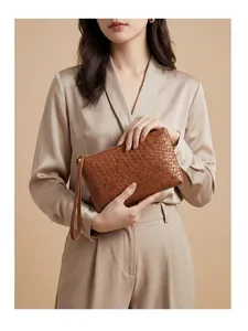 Detail of a brown woven leather clutch with a wrist strap and gold zipper accents