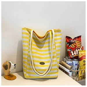Close-up of yellow and white striped canvas tote bag with metal logo and woven handles