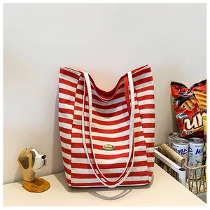 Detail of red and white striped canvas tote featuring a handmade metal emblem and strap
