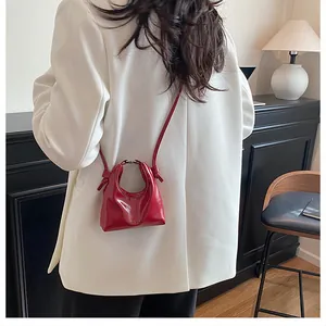 Detail of a bright red mini crescent handbag with shiny leather and knotted strap accents