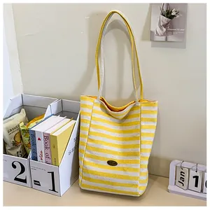 Detail of a yellow and white striped canvas tote bag featuring an oval brand logo plate
