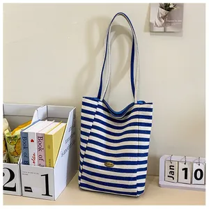 Close-up of blue and white striped canvas tote bag with oval metal logo plaque