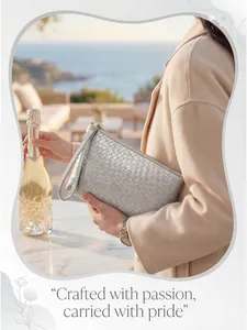 Silver woven clutch bag with zipper and wrist strap shown in a luxury seaside setting
