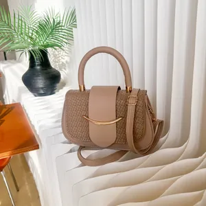 Taupe handbag with woven texture flap and gold hardware against wavy background