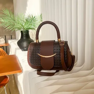 Elegant dark coffee brown handbag with gold metal detail on a decorative display stand