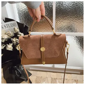 Detail einer braunen Handtasche mit gemischten Texturen und goldener runder Schnalle