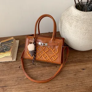 Brown faux leather crossbody bag with GA embroidery and crown detail on a wooden desk