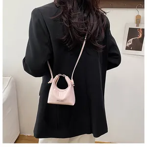 Pink patent leather mini crossbody bag with unique round handle worn on a black blazer