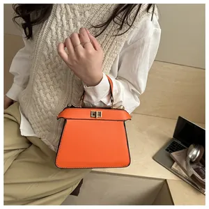 Detail einer leuchtend orangefarbenen Schultertasche mit goldener Schließe in Alltagsszene