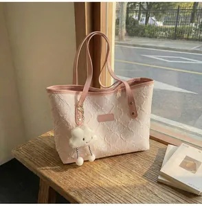 Detalle del bolso tote plisado rosa con colgante de nube de felpa en banco de madera