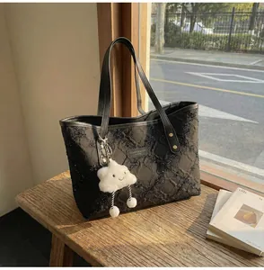 Detalle de bolso tote negro con lentejuelas y colgante de nube en un banco
