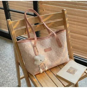 Detalle del bolso tote rosa claro con tejido plisado y colgante de nube de felpa blanca