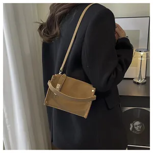 Sac bandoulière en daim marron avec fermoir doré porté par un mannequin en intérieur doux