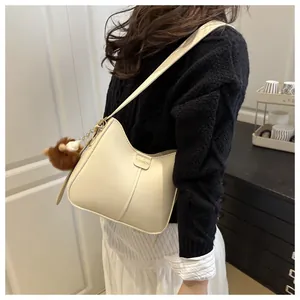 Detail of beige hobo bag with fashion logo tag and brown plush bear charm accessory