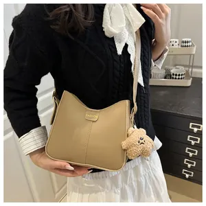 Close-up of beige hobo bucket bag with fashion label and brown plush bear charm