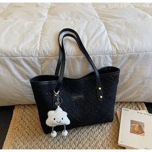 Detalle de bolso tote negro con relieve, placa de marca y colgante de nube decorativo