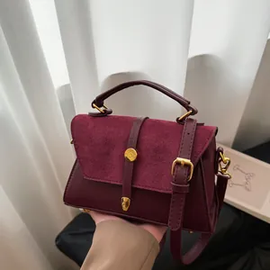 Elegante weinrote Handtasche mit goldener Schnalle und Wildlederdetail, handgehalten