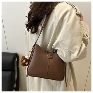 Detail of dark brown faux leather shoulder bag with plush charm and fashion logo