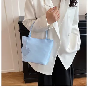Light blue tote bag with heart charm shown on model in white blazer and black pants