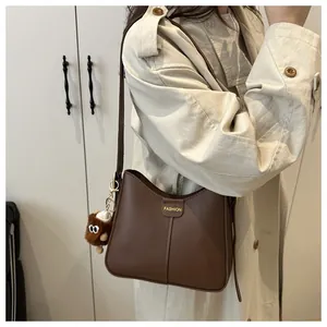 Brown faux leather shoulder bag with gold engraving and plush charm on trench coat
