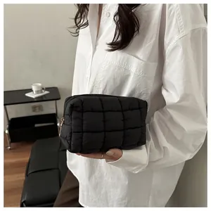 Detail view of a black quilted nylon cosmetic bag with golden zipper held by a model
