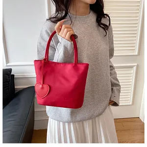 Red nylon tote bag with heart pendant detail and top handle held by a model