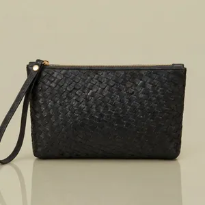 Classic black woven leather clutch with gold zipper and wristlet strap on reflective surface