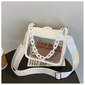 Detailed view of clear PVC square bag with white chain and adjustable strap on a table