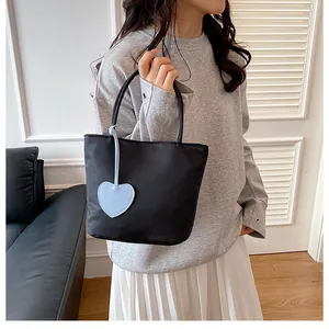 Detail of minimalist black nylon tote bag with a removable blue heart charm pendant
