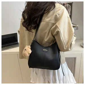 Detail of black matte leather shoulder bag featuring FASHION text and plush bear charm